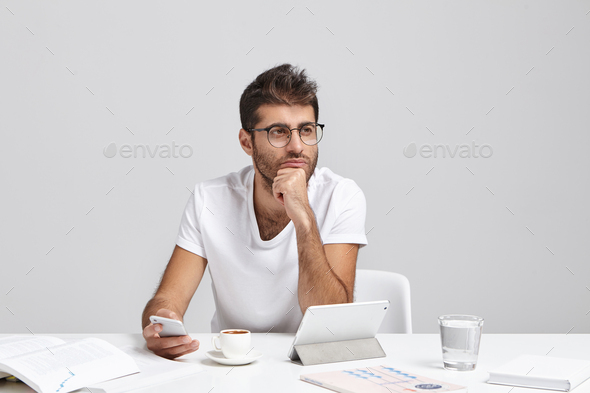 Thoughtful business worker tries to concentrate, holds mobile phone as waits for important call, dre
