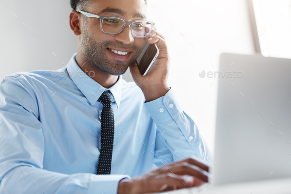 Young owner of company calling financial manager, having happy look in his notebook, being glad to s