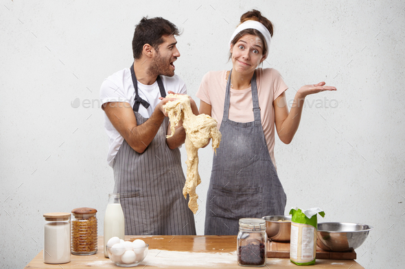 Puzzled woman shrug shoulders as holds dough, doesn`t know what she did wrong and angry chef shoutes
