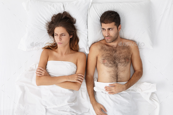 Picture of upset adult European couple having marital problems or disagreement lying side by side in