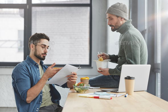 Business coworkers eat healthy lunch together at office, enjoy conversation, study documents, try to