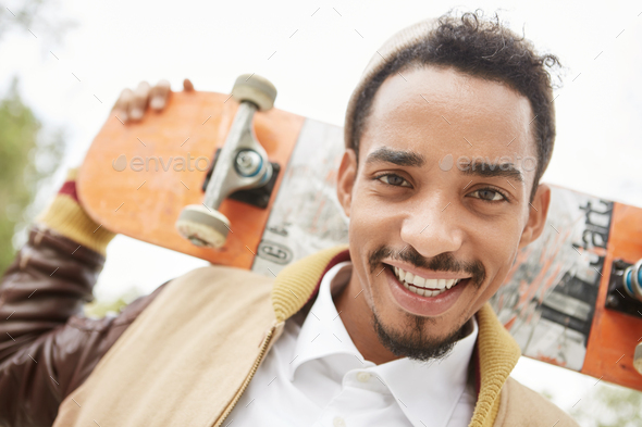 Skateboarding, sport, hobby and recreation concept. Relaxed smiling mixed race bearded teenager hold