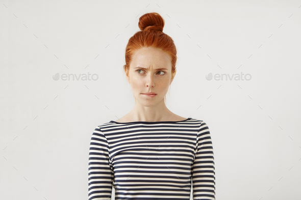 Pensive redhead woman with hair bun, curving her lips and raising eyebrows while thinking over or ma