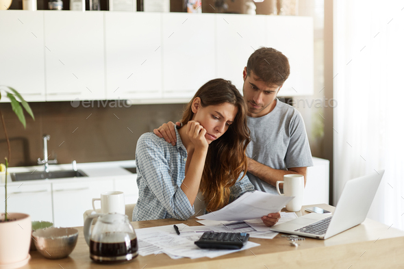 Beautiful young European couple feeling stressed out because of many debts, trying to make both ends