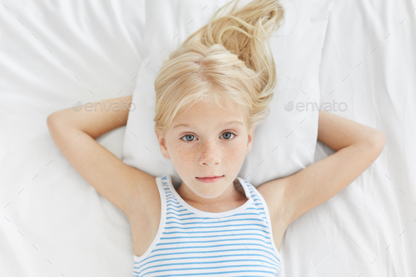 Pretty Blonde Freckled Blue Eyed Girl Lying In Bed On White Bedclothes Looking Directly Into