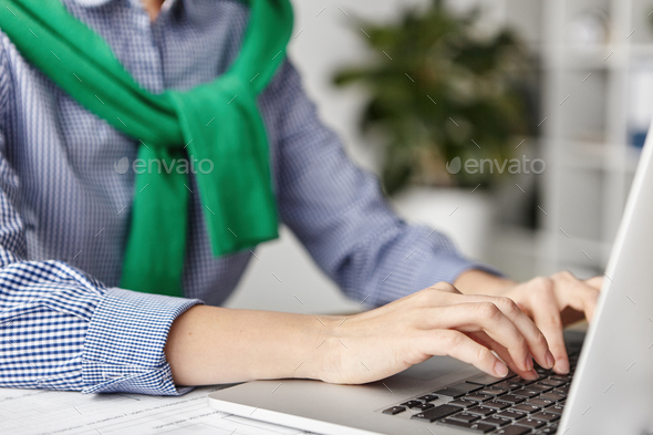 Cropped shot of female`s hands types or keyboards on modern laptop computer, checks emails or makes