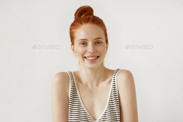 Good-looking young female with reddish hair tied in knot, having freckled pure healthy skin, wearing