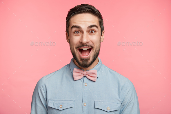 Emotive bearded man wears formal shirt and bow tie, happy to celebrate anniversary, invites friends