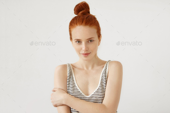 Studio shot of attractive woman with reddish hair knot and freckled skin, wearing striped loose T-sh