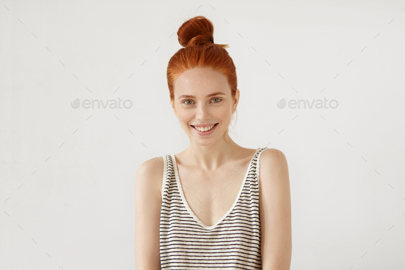 Happy freckled woman with red hair knot, wearing loose striped shirt, feeling relaxation while resti