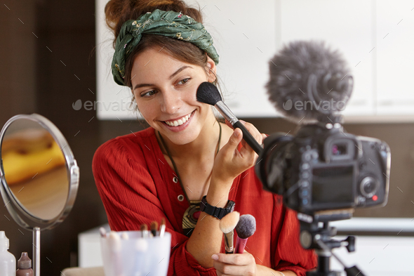 Portrait of beautiful smiling female vlogger makes video review, uses cosmetic product, records usef