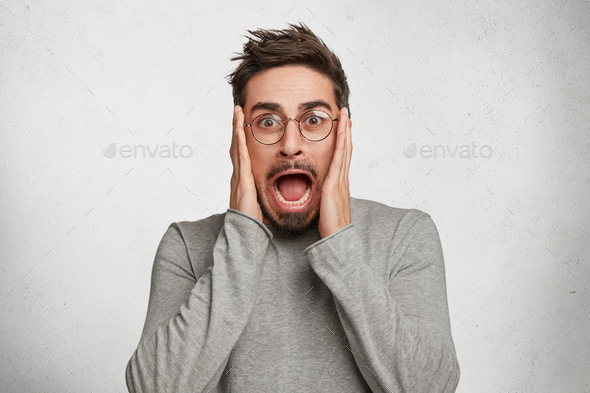 Omg, I don`t want to hear it. Shocked male has trendy hairdo, covers ears with hands, has frustrated