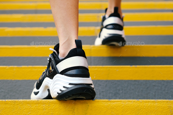 Close-up of sneakers on female legs on the stairs in the stadium, rear view.