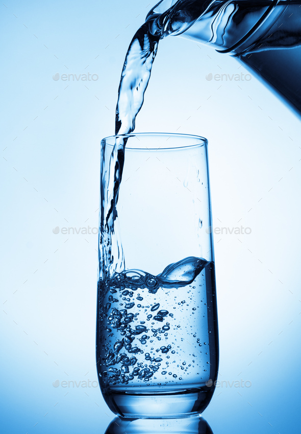 Pouring water from glass pitcher on blue background - Stock Photo - Images
