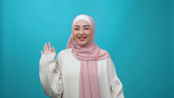Sociable Happy Young Muslim Woman in Hijab Smiling Friendly at Camera and Waving Hands Gesturing