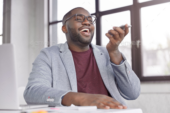 Cheerful dark skinned male makes voice call, happy to hear business partner, share financial news an
