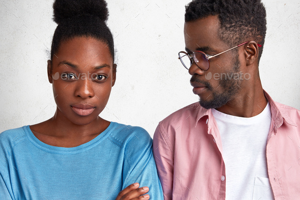 Young African couple sort out relationships. Discontent dark skinned woman looks seriously at camera