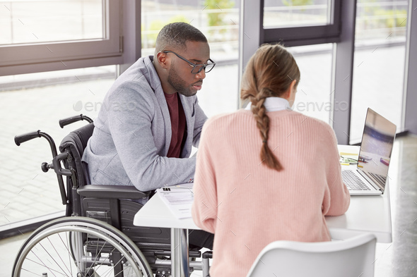 Serious dark skinned male invalid in wheelchair collaborates with young female, make business plan t