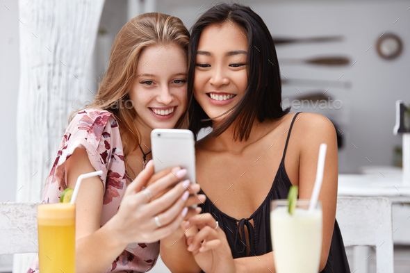 Photo of pleased mixed race women get good news on mobile phone, recieve email or make selfie with s