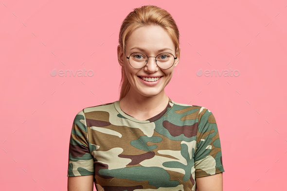 Blue eyed blonde positive woman in round spectalces, dressed casually, being in good mood after day