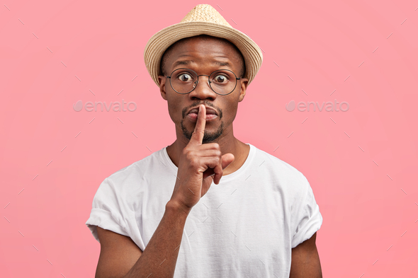 Be quiet and keep silence please! Funny stunned African American male shows hush sign, tells secret