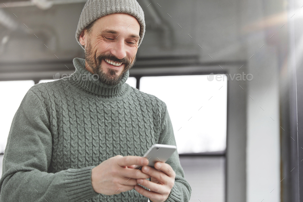 Attractive bearded male adult wears stylish knitted warm clothes analyzes latest news on social netw