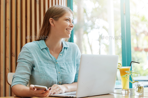 Cheerful attractive female copywriter earns money online, works remotely at laptop computer, holds m