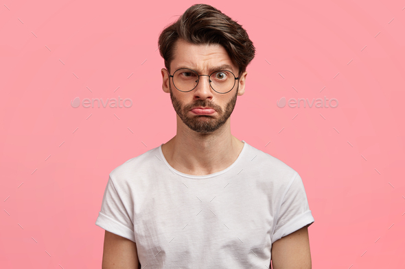 Serious discontent stylish male freelancer with unhappy expression, wears round spectacles, being an