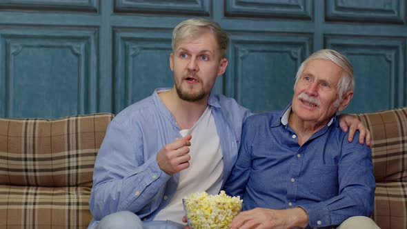 Family Senior Man Father and Adult Son Sitting on Sofa Watching Sport Game on TV with Eating Popcorn alt