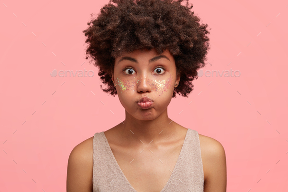 Funny amazed attractive African American female blows cheeks, has bated breath, cheeks decorated wit