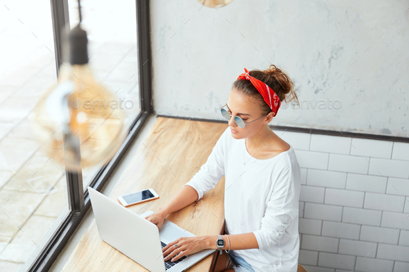 Stylish female freelancer in shades sends email message to customer, uses online application on lapt