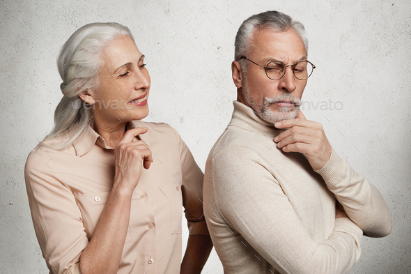 Abused angry elderly man in eyewear stands back to his wife, being upset after quarrel, have some mi