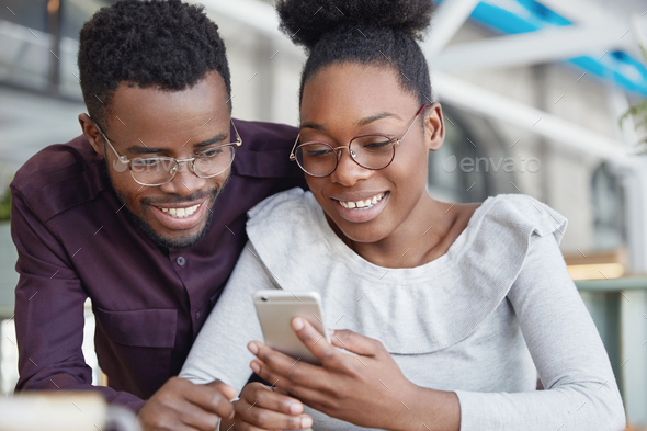 Lovely African couple browse internet on smart phone, book tickets online as going spend summer holi