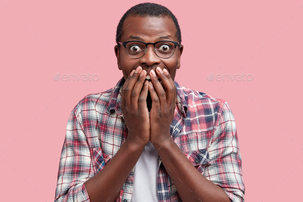 Portrait of overjoyed amazed African American male covers mouth, being overjoyed as recieves proposa