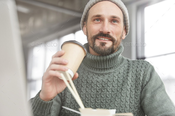 Close up portrait of handsome bearded skilled progranmer enjoys lunch break at office, eats fast foo - Stock Photo - Images