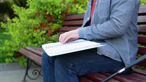 Blind Man Reading Braille Book Sitting on Bench in Summer Park alt