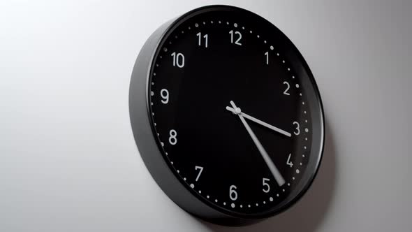 Black Clock Face In Time Lapse On White Wall alt