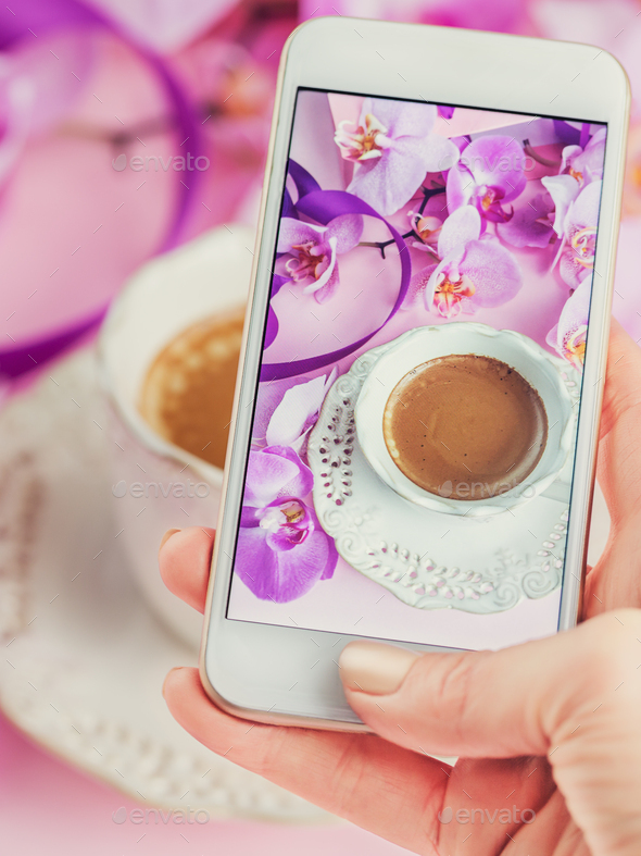 Woman taking picture of cup of coffe with pink orchids