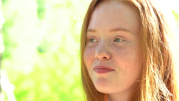 Portrait a Smiling Young Woman with Red Hair and Freckles Against the Backdrop of a Bright Sunny alt
