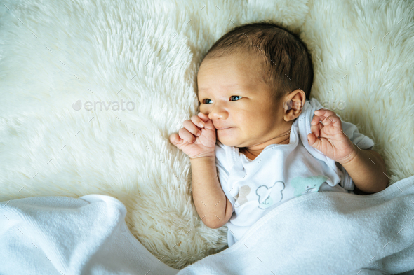 The newborn baby sleeps on the blanket and opens the eyes.