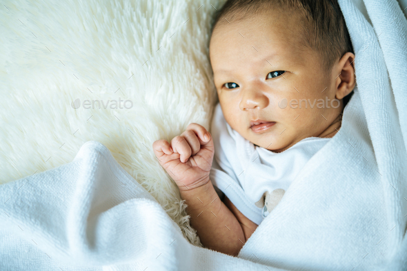 The newborn baby sleeps on the blanket and opens the eyes.