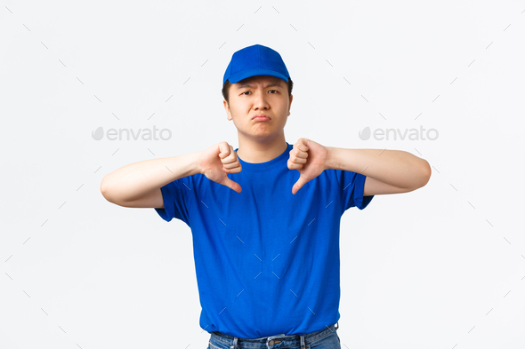 Disappointed grimacing asian delivery man in blue t-shirt and cap express dislike and bad attitude