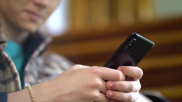 Teen Boy Sitting on Stairs at Home and Using App on His Mobile Phone alt