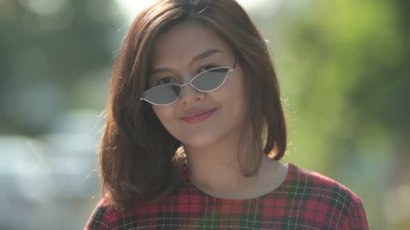 Face of Young Happy Asian Businesswoman with Sunglasses Smiling Outdoors alt