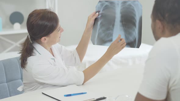 Doctor and Patient Examining Lungs X-ray in Hospital. African American Man and Caucasian Woman alt