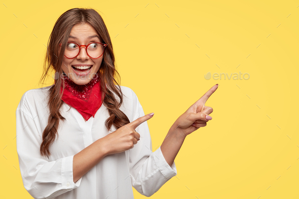 Studio shot of content woman with European appearance, has joyful expression, indicates with both in