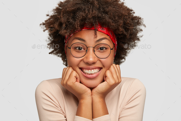 Close up portrait of happy black lady holds chin with both hands, glad that everything is okay, wear