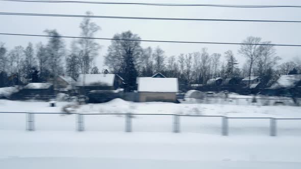 View From the Window of Moving Train on Snowcovered Village Onestorey Houses Fence Trees on Cloudy