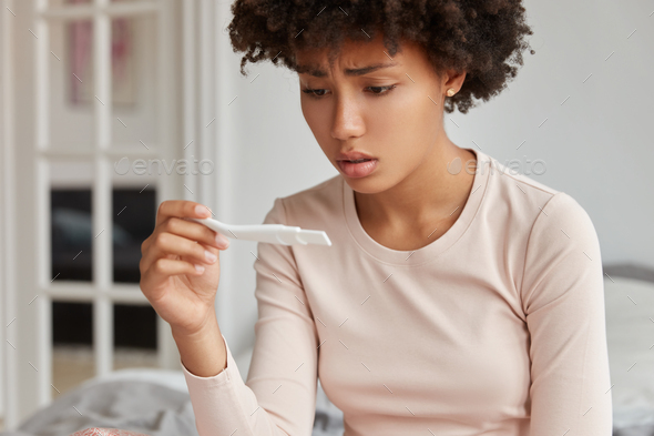 Depressed displeased dark skinned woman finds out about unwanted pregnancy, looks deperately at posi