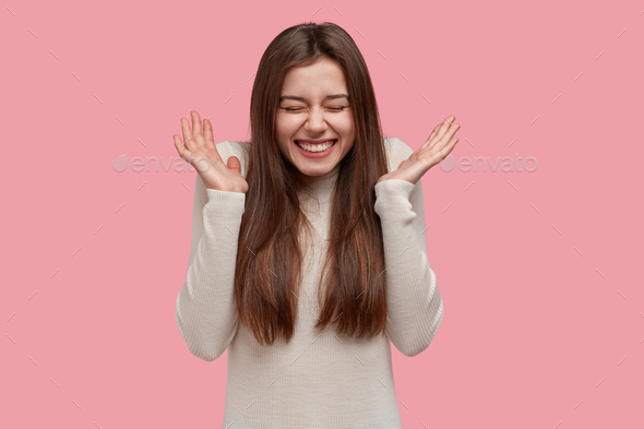 Overjoyed smiling lady spreads palms, expresses joy and happiness, asks to stop telling funny storie